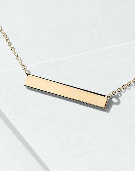 Birks Essentials gold bar necklace on a blue background.